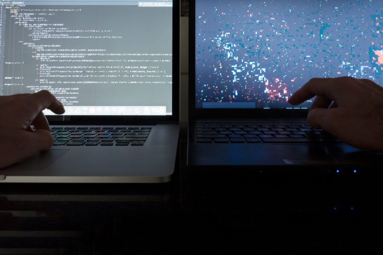 Dark room working with laptop computer screens hands on keyboards.