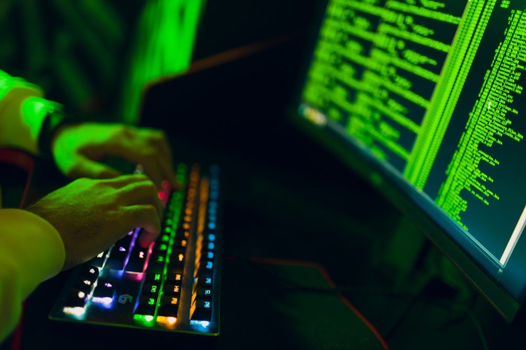 Hacker in hoodie working hacks code site on personal computer with green light