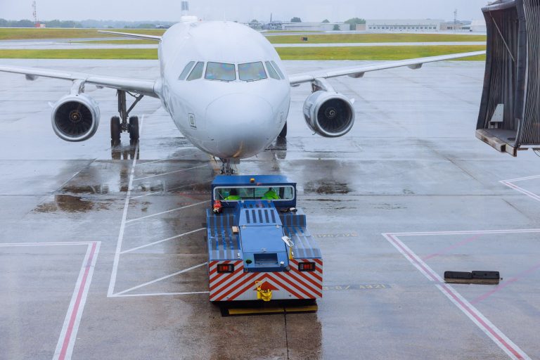 During rain, preparation for departure airplane is rolled out from terminal gate ready for a takeoff