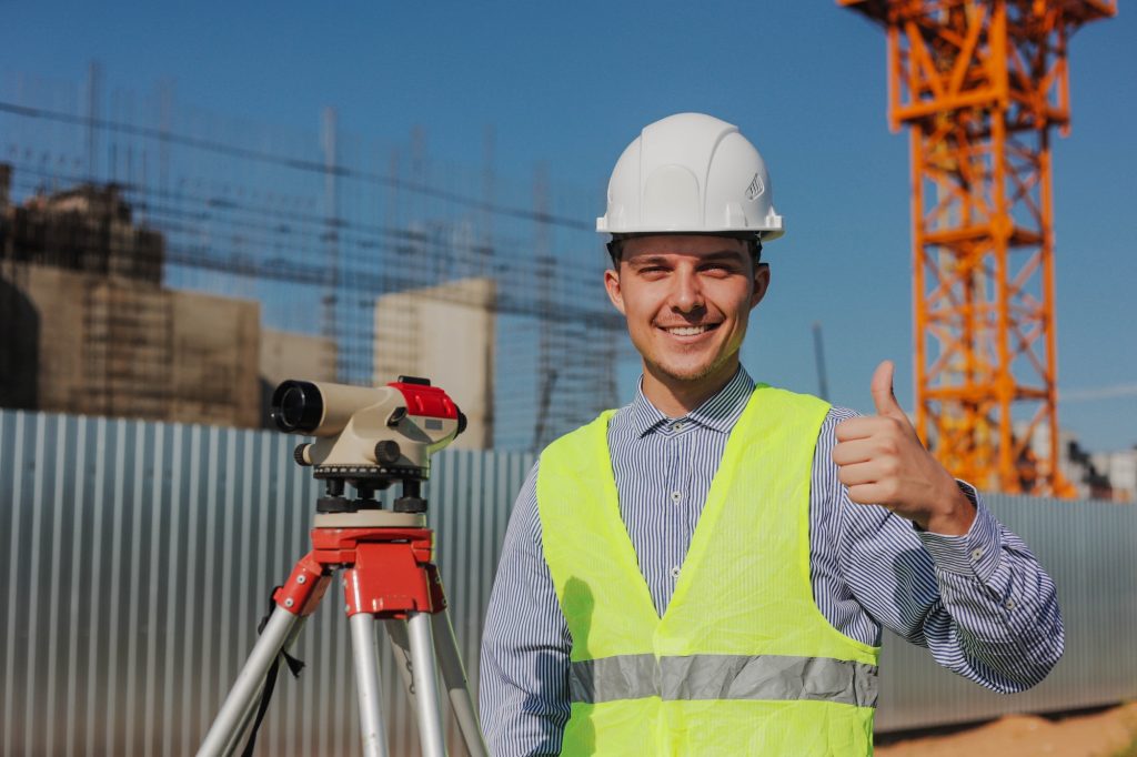 Happy engineer surveyor with survey camera showing thumbs up