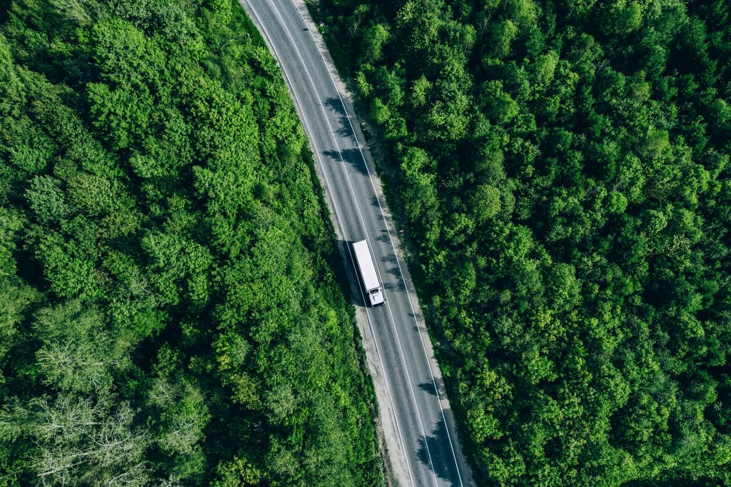 Aerial drone view of truck car on green summer curved road. Transportation and logistics concept.