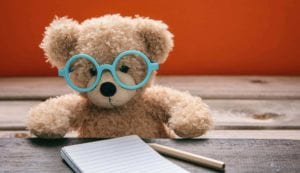 Cute teddy wearing glasses doing homework. Back to school