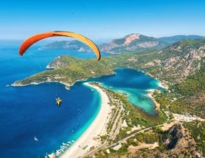 Paraglider tandem flying over the sea with blue water and mountains