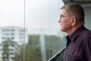 Profile view of old man thinking while looking outside glass window of modern building