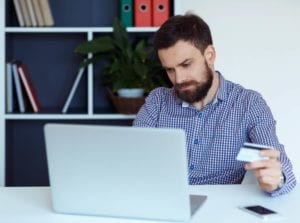 Young bearded man pays by credit card online shopping