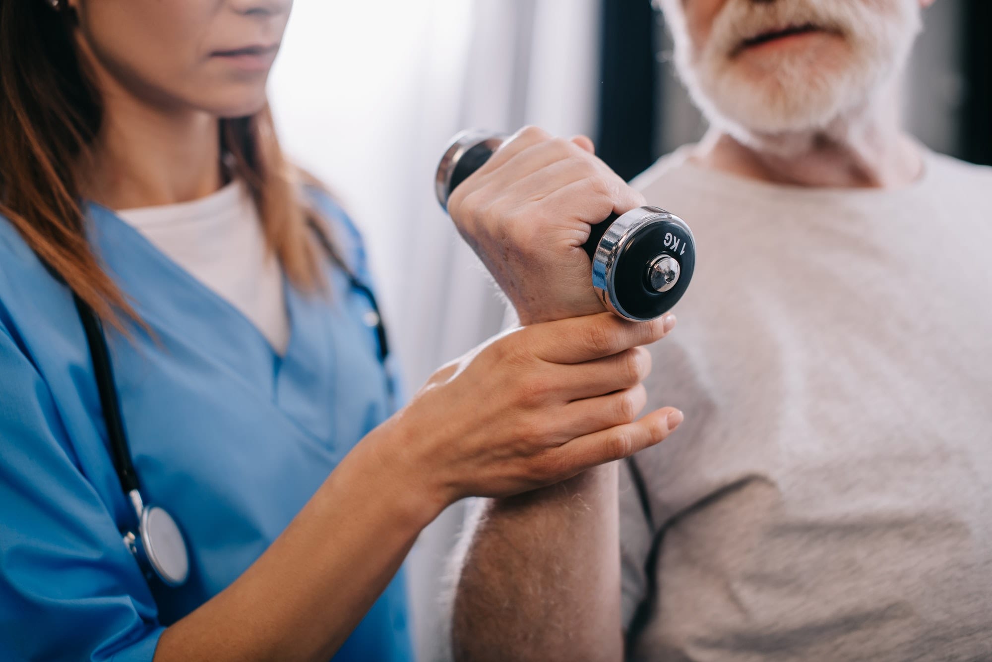 Old man with dumbbell and nurse during physiotherapy